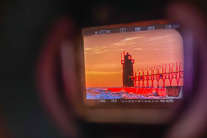 Looking through the viewfinder of a Sony A7R3 shows settings and image of a lighthouse at sunset