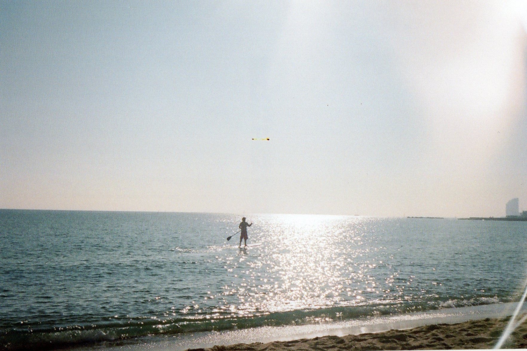 a standup paddle boarder paddles into the sun 