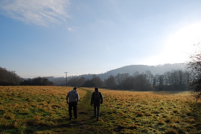 two friends walk along a dirt path that runs through a grassy field 