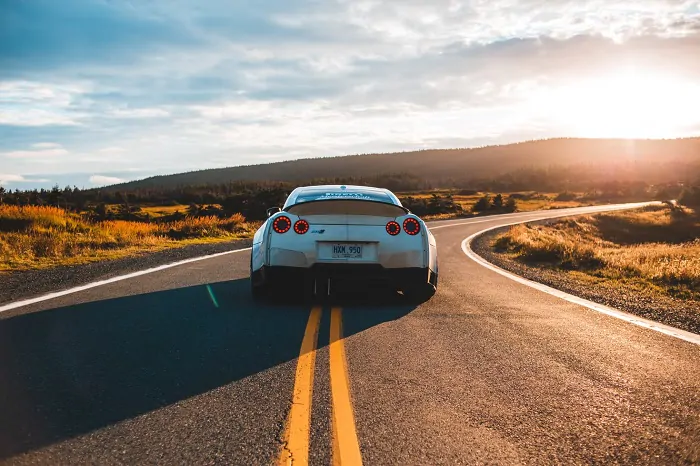 White sports car driving in the middle of the road at sundown