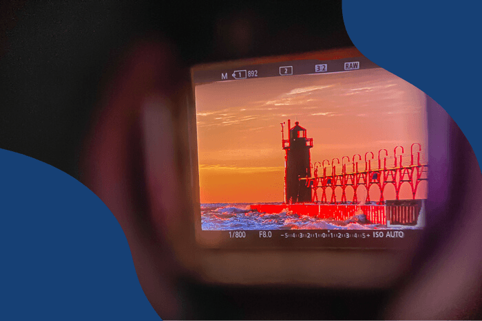Looking through the viewfinder of a Sony A7R3 shows settings and image of a lighthouse at sunset