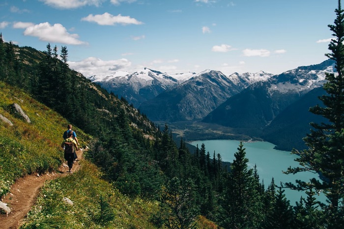 Two hikers on a mountain trail with lake and mountains in the background