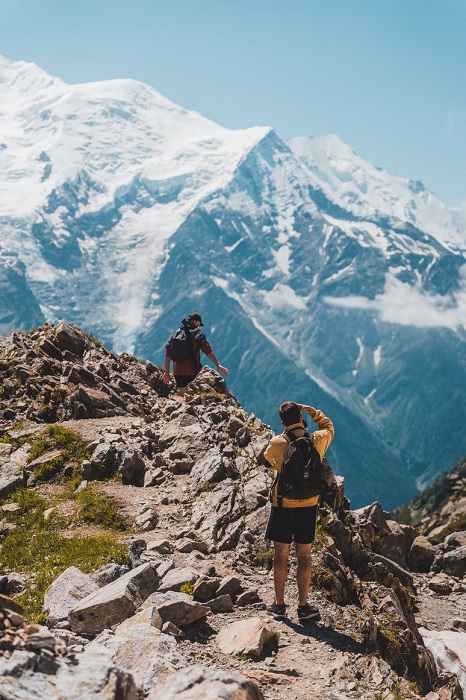 Two hikers walking a rocky mountain ridge, one taking a snap with one of the best lightweight cameras