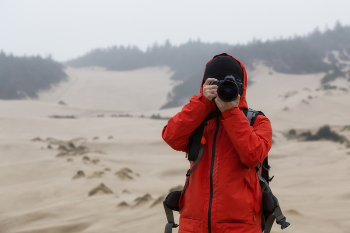 Man in red jacket shooting with one of the best DSLR cameras with weather sealing on a beach