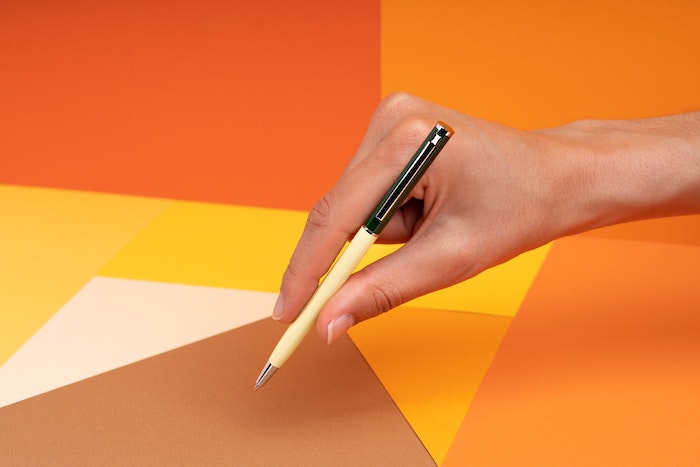 model holding a pen with orange paper in the background 