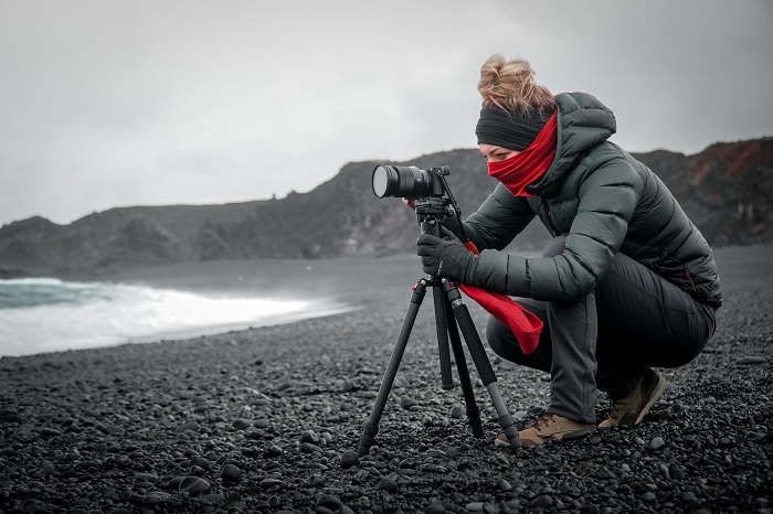 Woman setting up a camera on a tripod on a cold beach