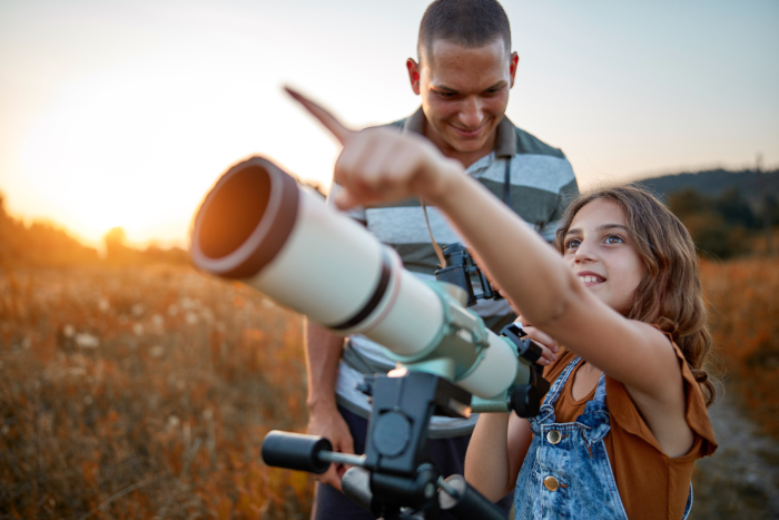 Father and daughter at sunset with a telescope