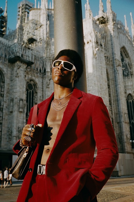 Man in red cord jacket with no shirt outside a cathedral