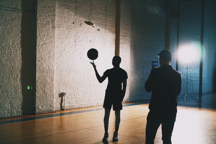 Silhouettes of a person recording a basketball player spinning a basketball