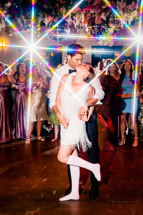 Wedding portrait of a couple kissing on the dance floor with wedding guests in the background by Kari Bjorn Thorleifsson