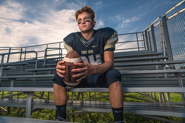 Senior portrait of a high-school football player sitting in the stands holding a football