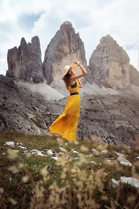 Portrait photo of a model in yellow standing on grass with jagged mountains in the background