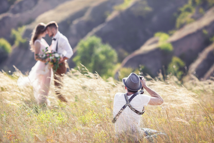 A professional wedding photographer takes pictures of the bride and groom in nature