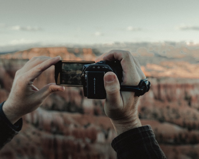 A person holding up a camcorder to record a canyon landscape