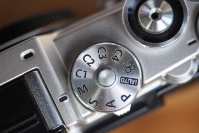 Dial mode and shutter button on silver mirrorless camera.