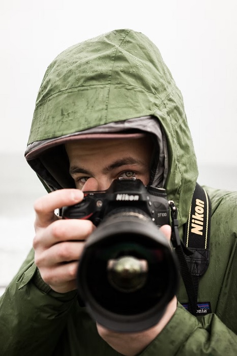 Photographer in a rain coat lifting a Nikon camera to his face