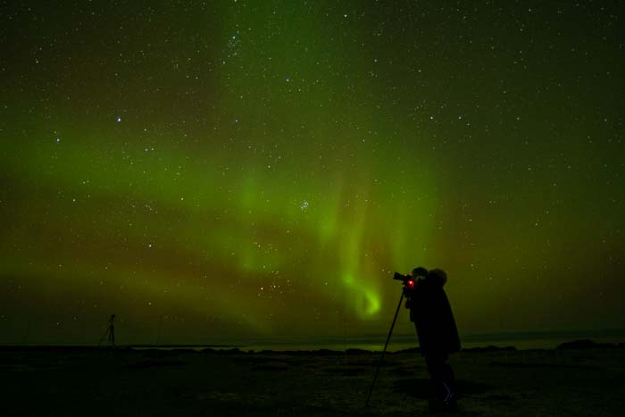 A photographer taking a picture against the Northern Lights with stars in the sky
