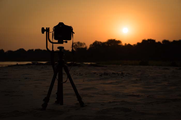 Silhouette of a tripod set up to shoot a sunset on a beach with best settings for sunset photos
