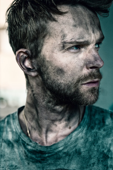 A close-up portrait of a man looking sideways with grease on his face and shirt