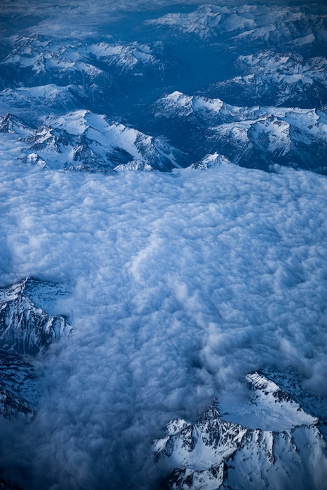 An aerial photo of clouds and snow-capped mountains from an airplane