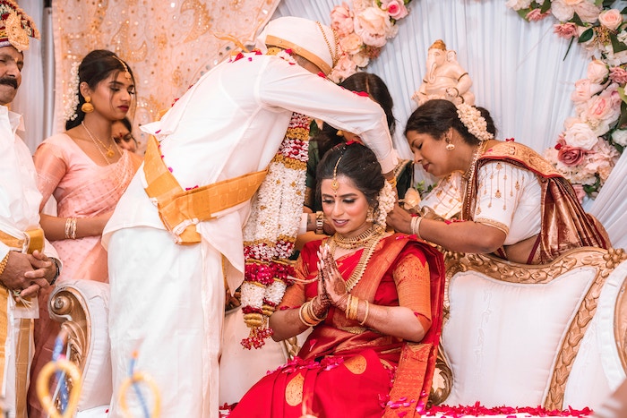 A bride in traditional Indian wedding clothing and makeup sitting and being attended to by others