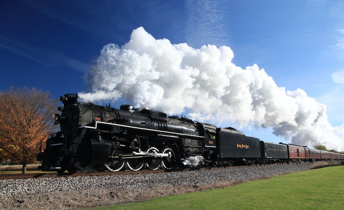 A black, old-fashioned locomotive train with white smoke billowing out