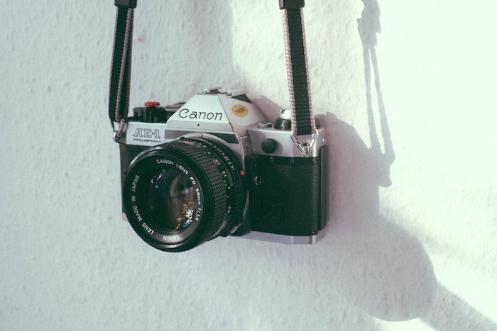 A Canon AE-1 camera hanging against a white wall by its strap