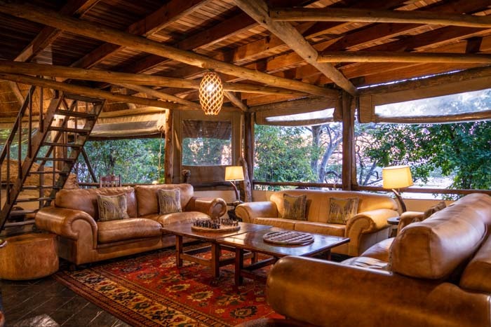 HDR image of a living room in a safari lodge with furniture, a wood ceiling, and windows