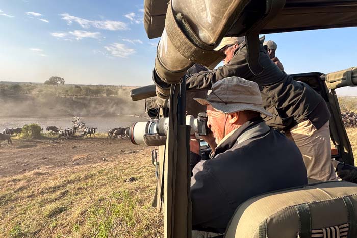 Photographer sitting in a safari jeep taking wildlife photos using one of the best Sony E-mount lenses, the 70-200mm
