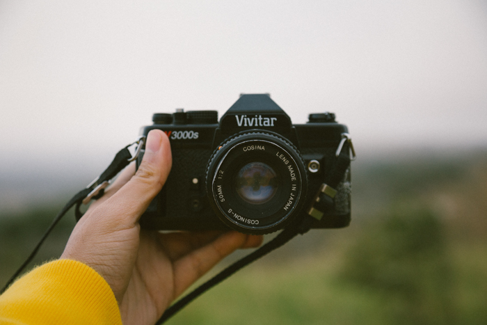 a photographer with an outstretched arm holds a Vivitar camera towards the camera taking the photo
