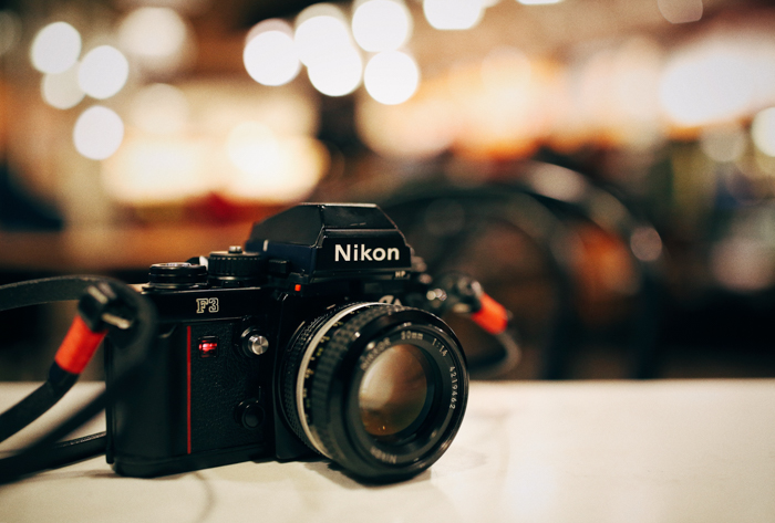  a nikon camera sits on a table in front of a well-lit background