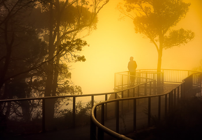 A person on a bridge in a foggy landscape at sunset