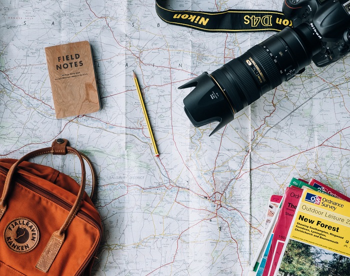 A travel photographers camera, bag and notebook on a map