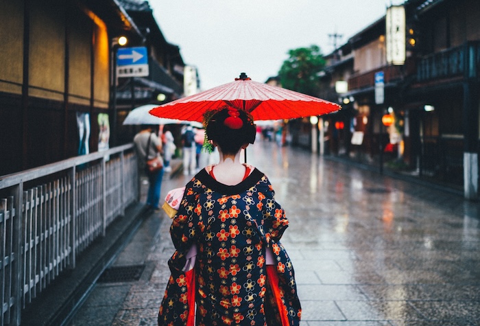 A geisha in traditional clothing holding an umbrella on a rainy street
